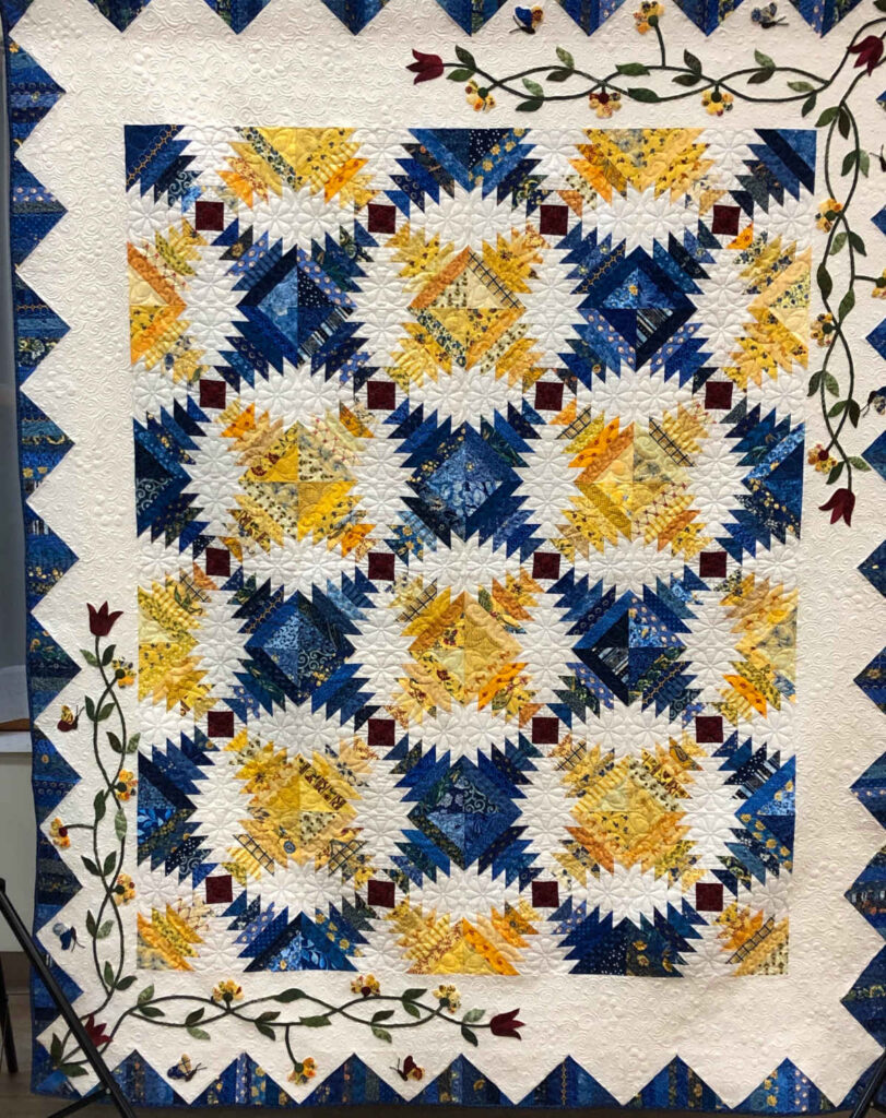 The 2023-2024 AQG Raffle Quilt. "Le Papillon" is a traditional pineapple block with a country French border. Pieced by AQG members Karen Acosta, Sue Cochrane, Carolyn Dixson, Jane Mullenix, Dawn Ott, Adrienne Randall and Polly Schatz. Applique border by Janice Reece. Custom quilting by Kate Gollsneider and Rebecca Musliner.